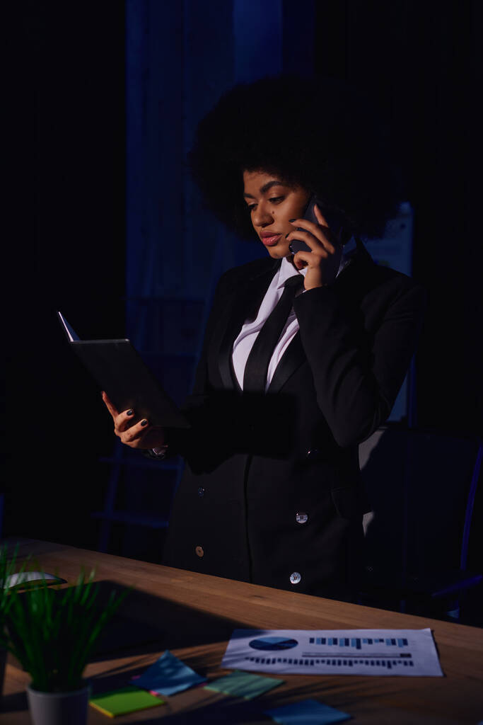 african american businesswoman with notebook talking on smartphone while working in office at night - Photo, Image