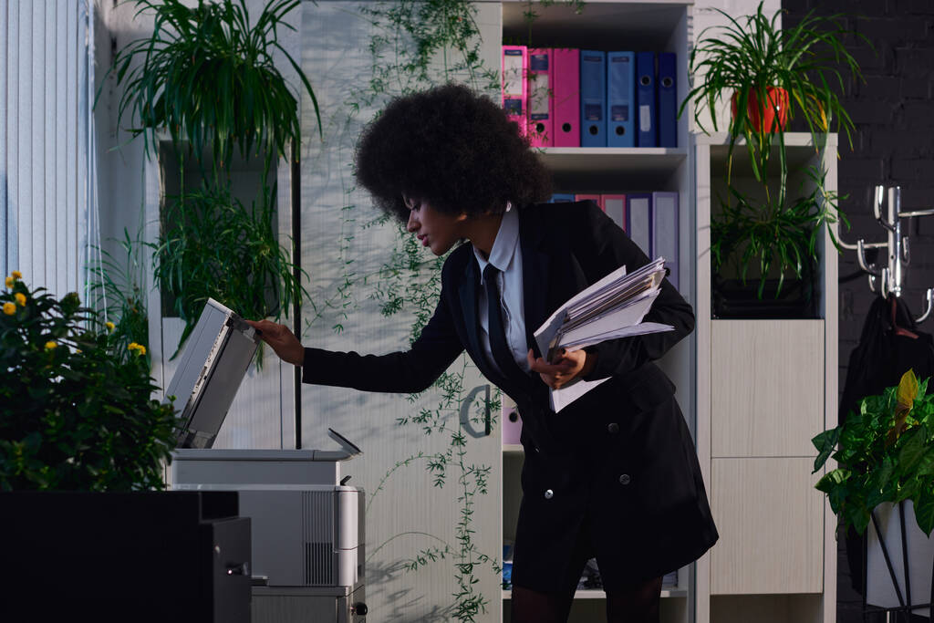 elegante mujer de negocios afroamericana con la máquina fotocopiadora de apertura de documentos en la noche en la oficina - Foto, imagen