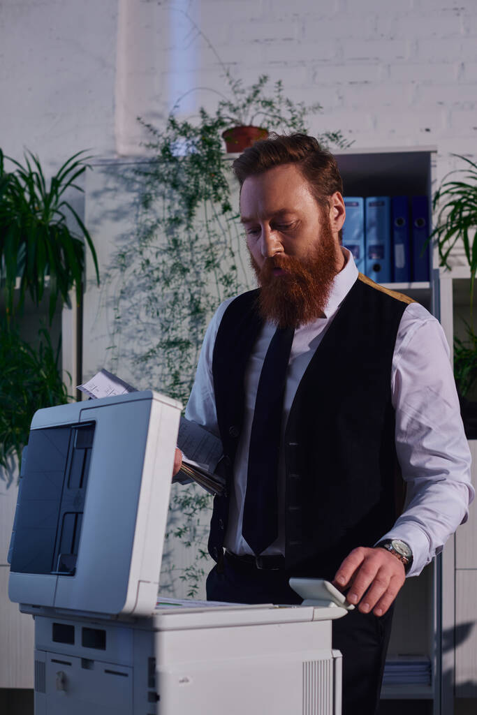 homem de negócios barbudo focado copiar documentos na máquina copiadora enquanto trabalhava até tarde no escritório - Foto, Imagem