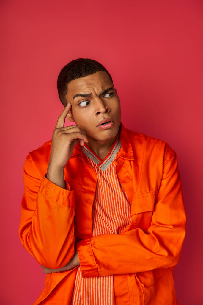 preoccupato e teso afroamericano uomo in camicia arancione guardando lontano su sfondo rosso - Foto, immagini