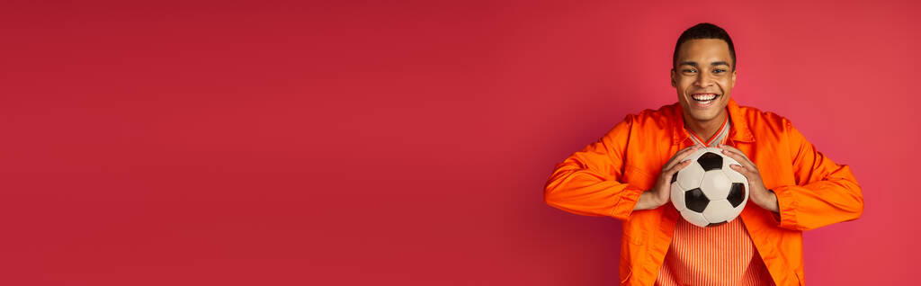 赤,バナー,コピースペースにサッカーボールを保持するオレンジ色のシャツのハッピーアフリカ系アメリカ人男性 - 写真・画像
