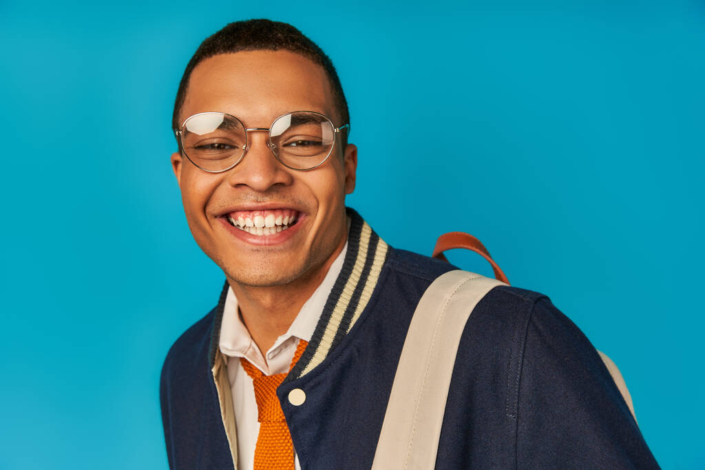задоволений афроамериканський студент в окулярах і модний піджак посміхається на камеру на синьому, портрет - Фото, зображення