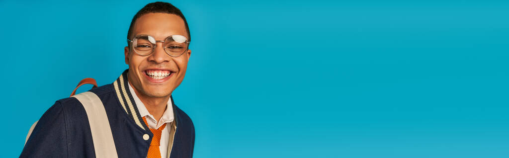 šťastný africký americký student ve stylové bundě a brýlích na modrém, banner, kopírovací prostor - Fotografie, Obrázek