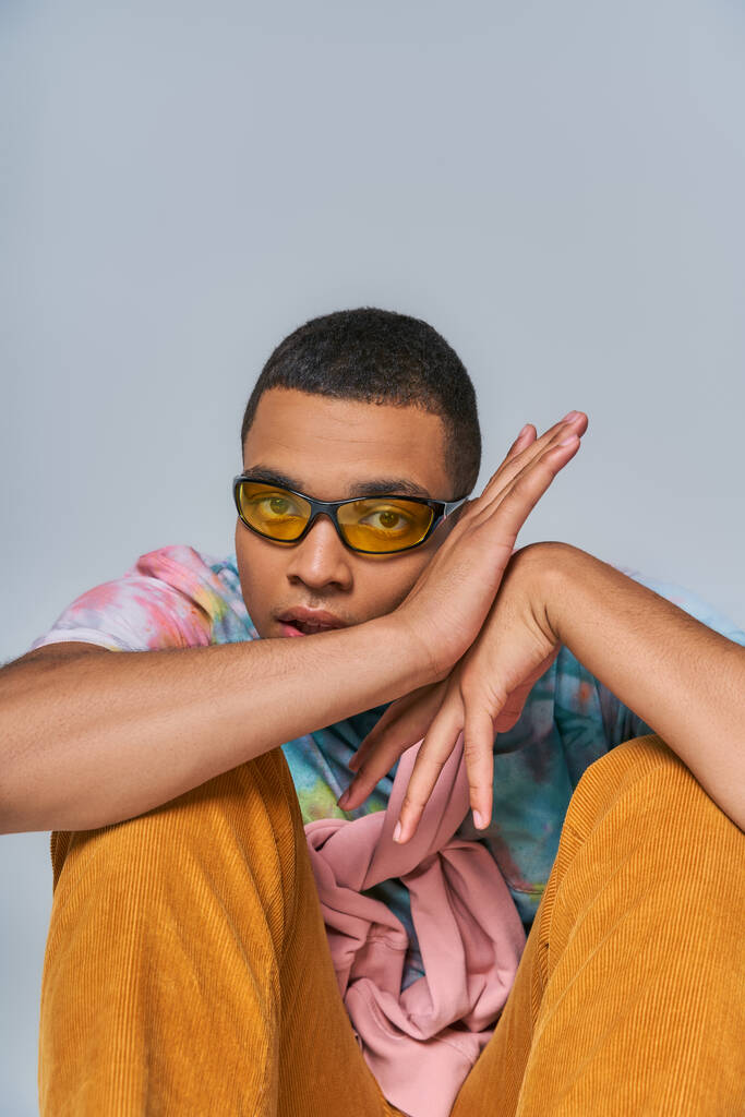 Moda gözlüklü, kravat boyalı tişörtlü, gri renkli kameraya bakan Afro-Amerikan bir adam. - Fotoğraf, Görsel