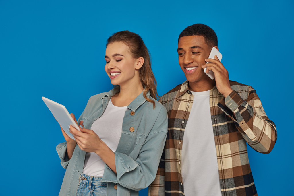 heureux couple interracial à l'aide de gadgets sur fond bleu, homme afro-américain ayant appel téléphonique - Photo, image