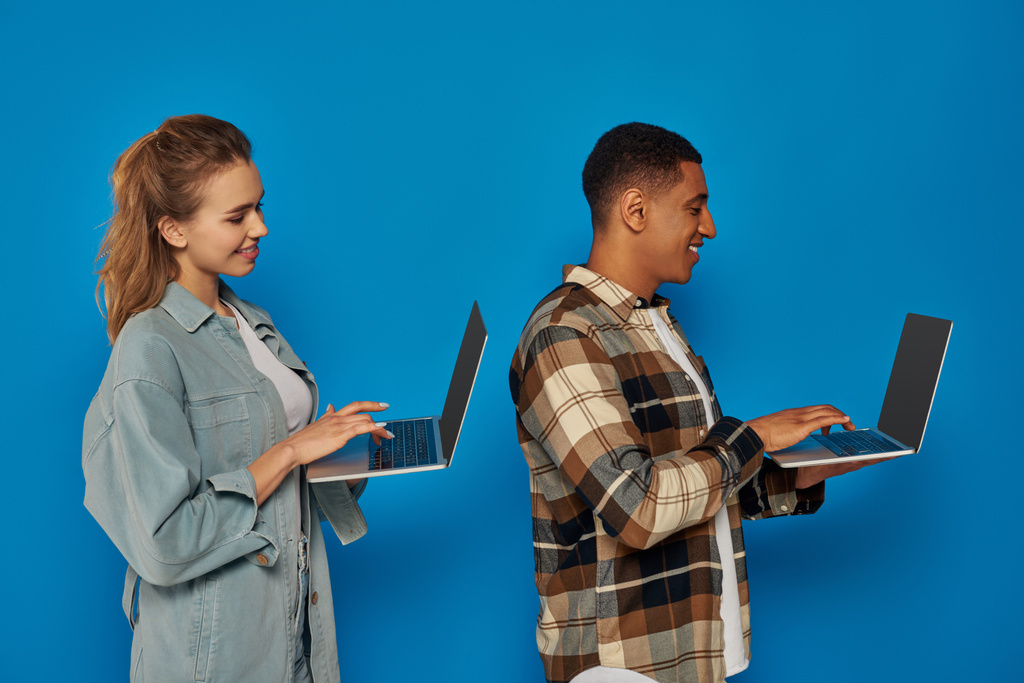 Ευτυχισμένοι διαφυλετικοί ελεύθεροι επαγγελματίες που χρησιμοποιούν φορητούς υπολογιστές σε μπλε φόντο, διαφορετικοί πολιτισμοί άντρας και γυναίκα, πλευρά - Φωτογραφία, εικόνα