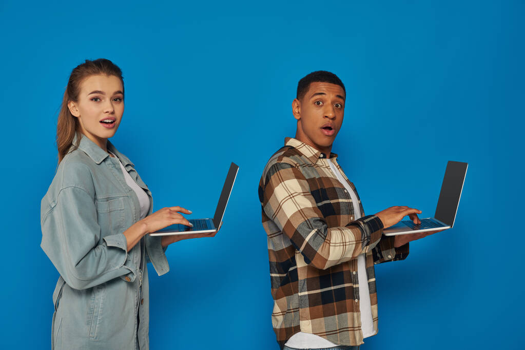 здивовані міжрасові фрілансери, використовуючи ноутбуки на синьому фоні, різноманітні культури чоловік і жінка - Фото, зображення