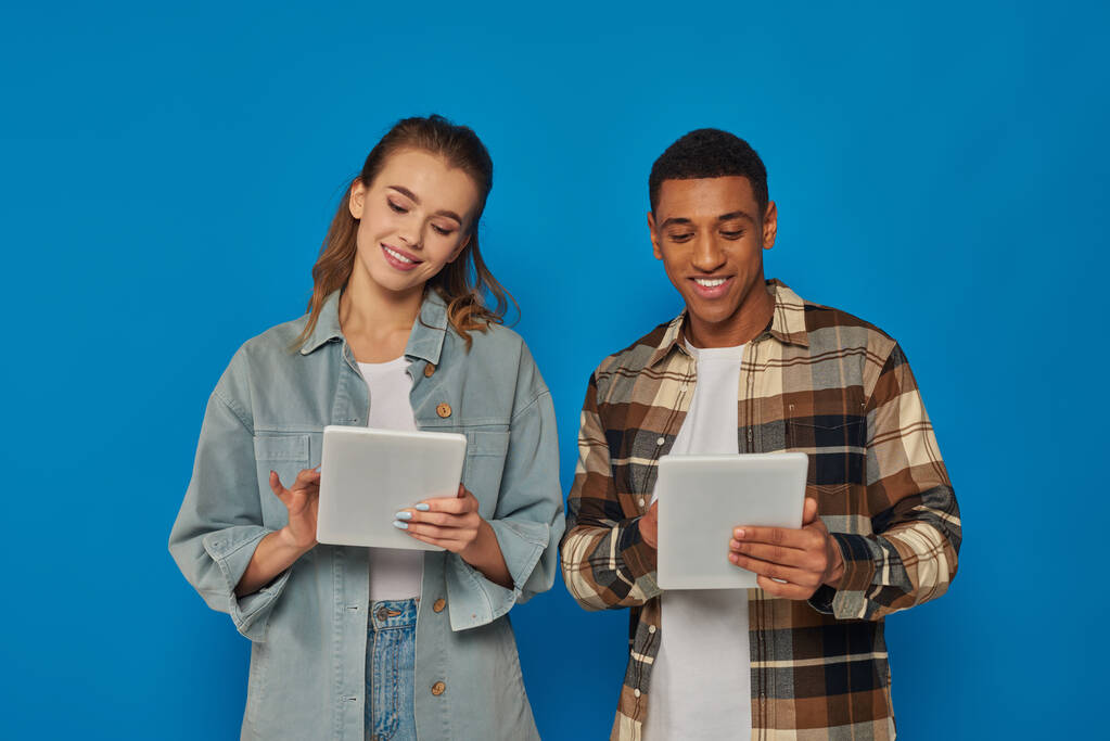 szczęśliwy międzyrasowy mężczyzna i kobieta za pomocą cyfrowych tabletek na niebieskim tle, social media i networking - Zdjęcie, obraz