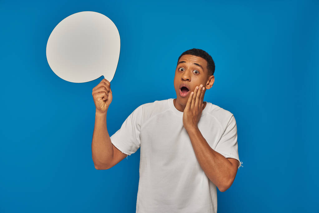verbijsterd afrikaanse amerikaanse man met open mond houden blanco spraak zeepbel op blauwe achtergrond - Foto, afbeelding