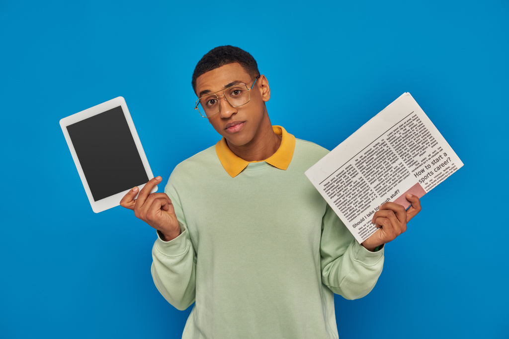 pohledný africký Američan v brýlích drží digitální tablet a noviny na modrém pozadí - Fotografie, Obrázek