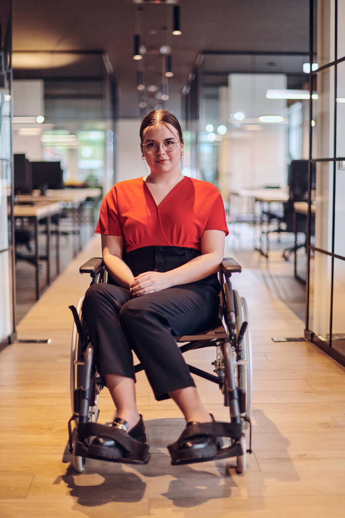 Nowoczesna młoda bizneswoman na wózku inwalidzkim otoczona jest przestrzenią roboczą z przeszklonymi biurami, uosabiającą determinację i innowacyjność w świecie biznesu.. - Zdjęcie, obraz
