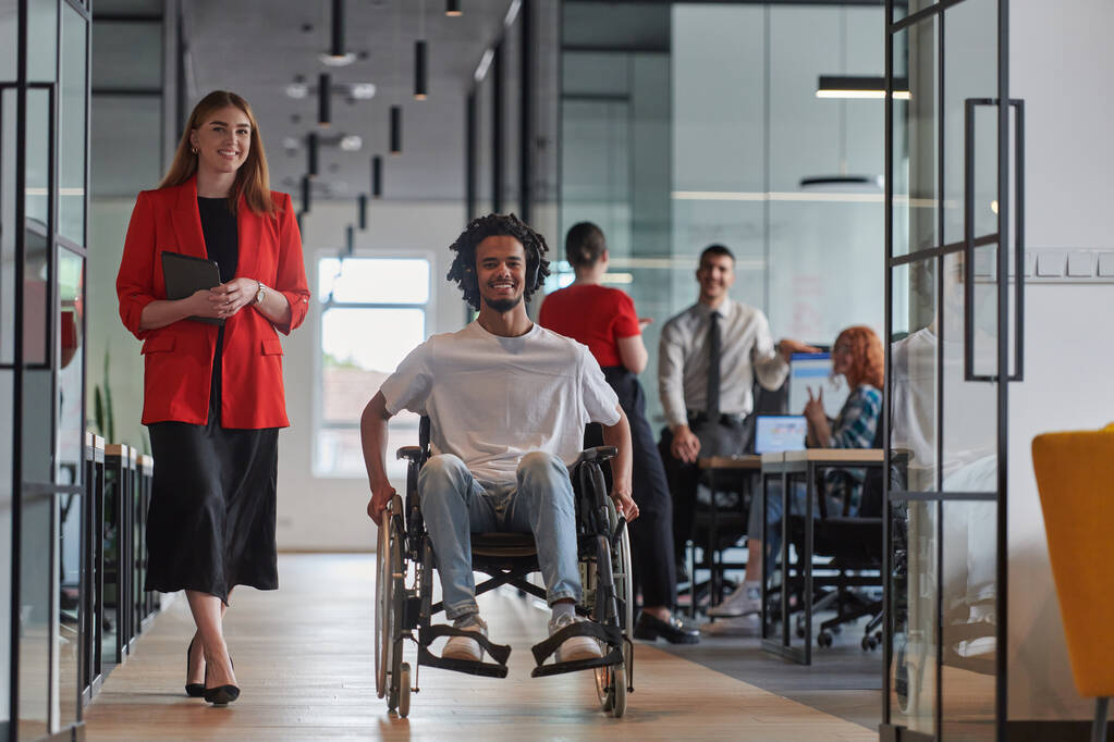 Skupina mladých podnikatelů v moderní prosklené kanceláři zachycuje podstatu rozmanitosti a spolupráce, zatímco dva kolegové, včetně afroamerického podnikatele na invalidním vozíku - Fotografie, Obrázek