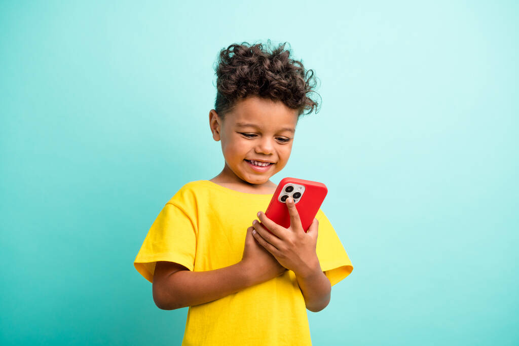 Foto de estudante inteligente com cabelo castanho vestido camiseta amarela olhar para smartphone conversando isolado no fundo cor turquesa. - Foto, Imagem