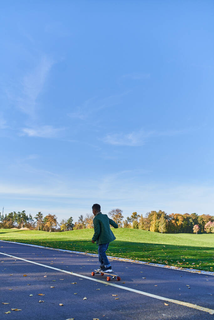 schattig jongetje in buitenkleding berijden penny board, asfalt, park, herfstseizoen, kid in herfstkleding - Foto, afbeelding