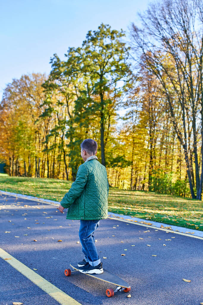 niño en ropa de abrigo otoñal a caballo penny board, asfalto, parque en temporada de otoño, hojas de oro, lindo niño - Foto, imagen
