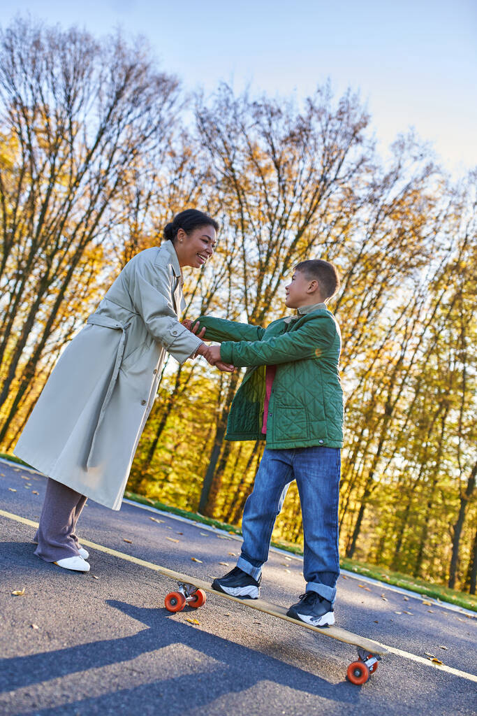 happy childhood, african american mother and son on penny board, woman and boy, hold hands, autumn - Photo, Image