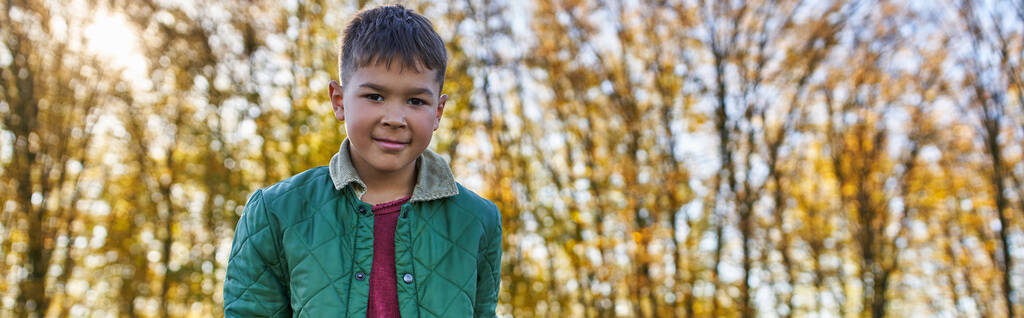 happy african american boy in outerwear looking at camera in autumn park, fall season, banner - Photo, Image