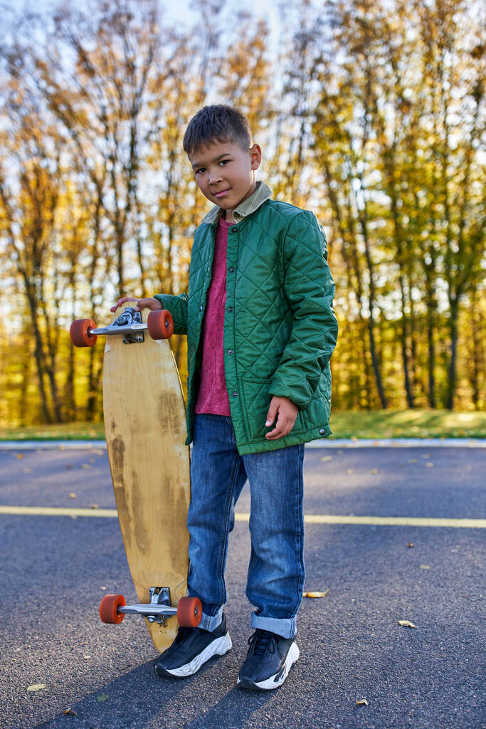 volledige lengte, schattig Afrikaans amerikaans jongen in buitenkleding holding penny board, herfst park, herfst seizoen - Foto, afbeelding