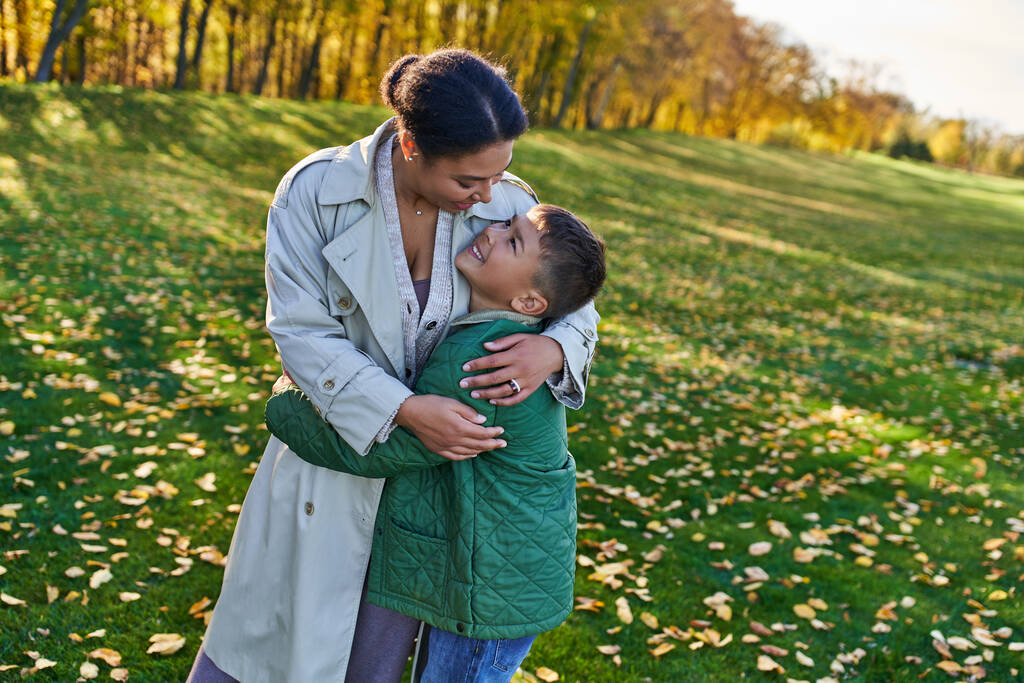 šťastná africká americká žena objímající se synem, stojící u zlatých listů, podzim, mateřská láska - Fotografie, Obrázek