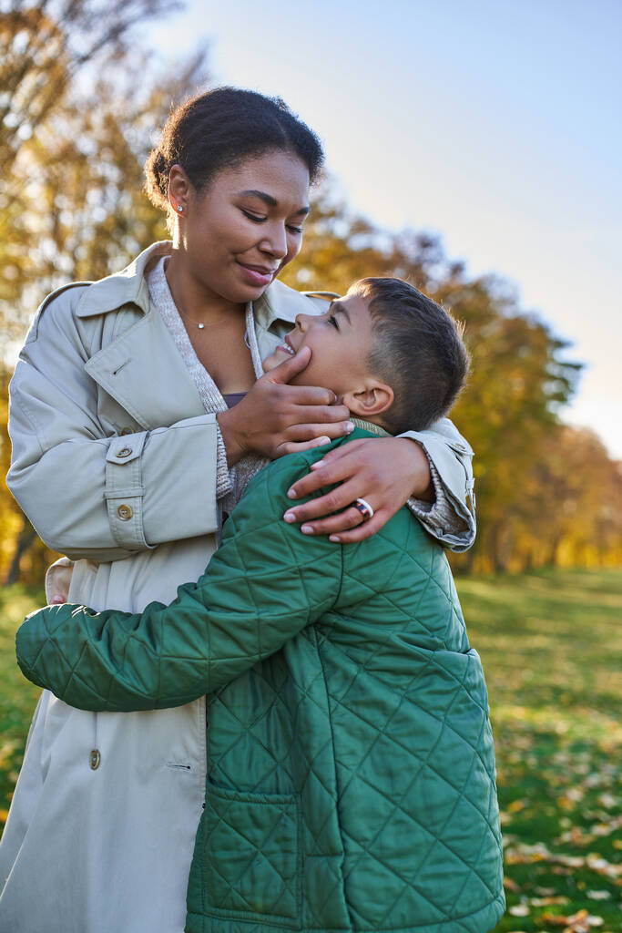 motherly love, joy, african american woman hugging with son, standing near golden leaves, autumn - Photo, Image