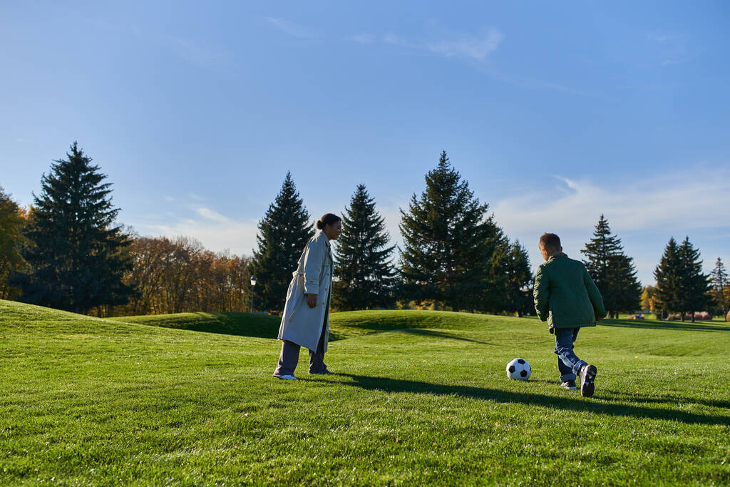 veselý africký americký chlapec hraje fotbal se šťastnou matkou na zelené louce, fotbal, podzim, běh - Fotografie, Obrázek