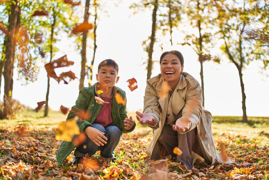 Χαρούμενες αναμνήσεις, χαρούμενη μητέρα και γιος ρίχνουν φθινοπωρινά φύλλα, φθινοπωρινή εποχή, αφροαμερικάνικη οικογένεια - Φωτογραφία, εικόνα