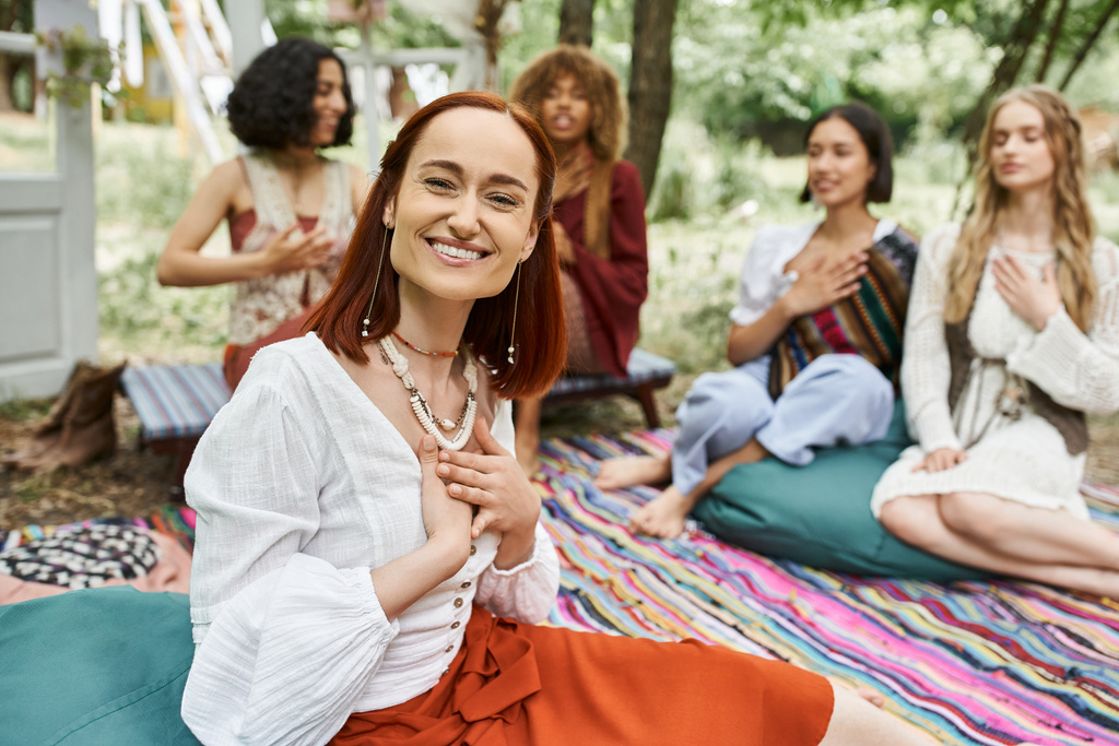 smiling and trendy redhead woman sitting near blurred multiethnic friends in retreat center - Photo, Image