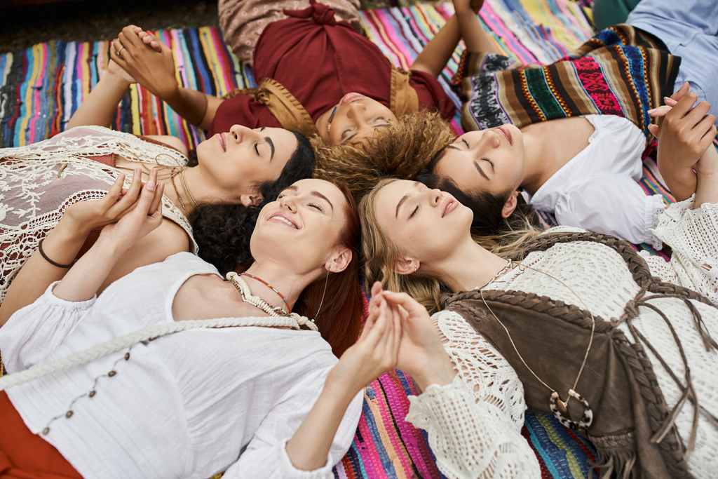 веселые многонациональные женщины с закрытыми глазами, держась за руки, одеяло, на открытом воздухе, центр отдыха - Фото, изображение