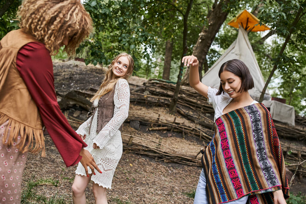 молодые и межрасовые девушки в костюмах бохо, танцующие на лужайке в центре отдыха - Фото, изображение