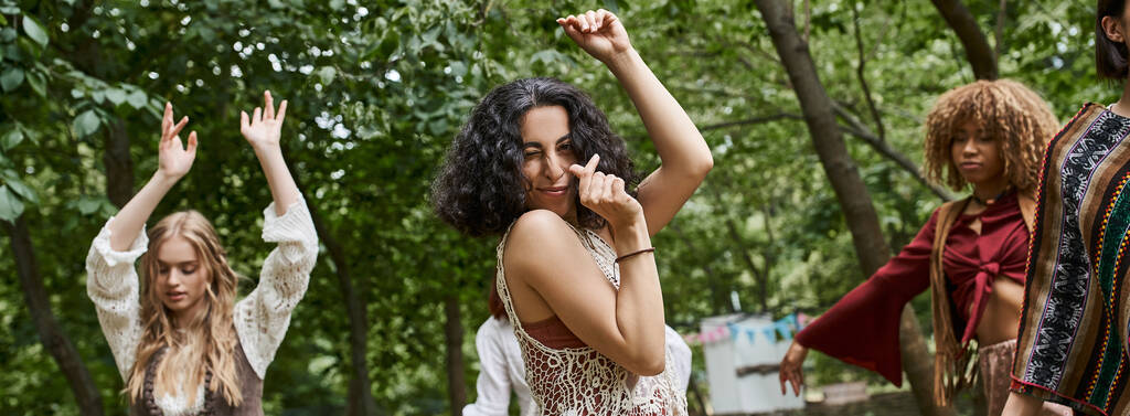 позитивна багаторасова жінка танцює біля розмитих подруг на відкритому повітрі в центрі відпочинку, банер - Фото, зображення