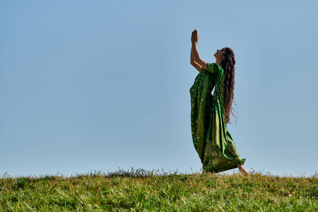 Yaz neşesi, otantik elbiseli Hintli kadın, dua eden elleri mavi gökyüzünün altındaki yeşil çimlerde. - Fotoğraf, Görsel