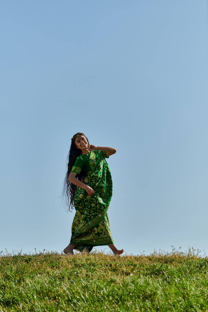 летний отдых, беззаботная индианка в сари ходит по зеленому лугу под голубым безоблачным небом - Фото, изображение