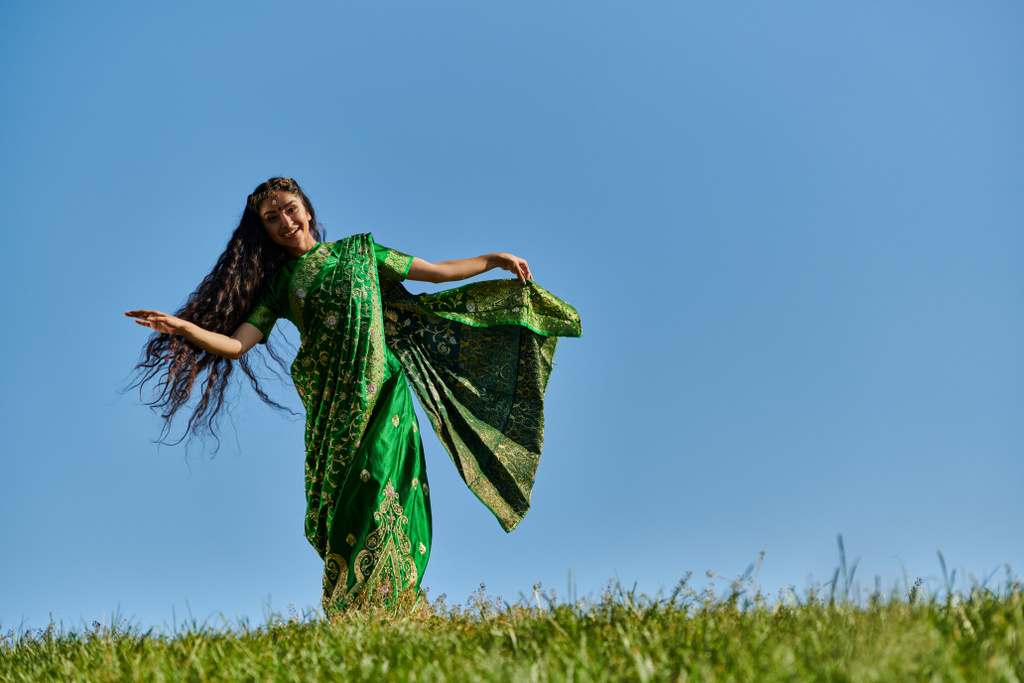 青空の下の緑のフィールドで伝統的な服装で陽気なインドの女性の夏のダンス - 写真・画像