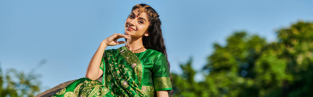 Yeşil sari giymiş gülümseyen Hintli kadın ve arka planda gökyüzü olan Matha Patti, afiş. - Fotoğraf, Görsel