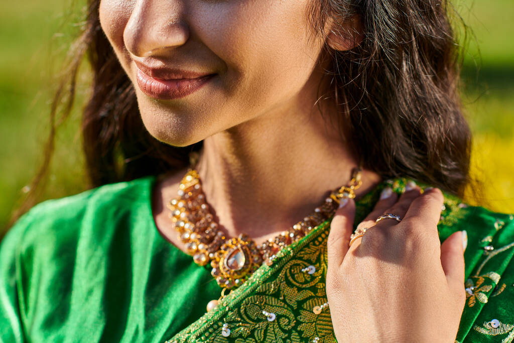 καλλιεργημένη θέα χαμογελαστή νεαρή γυναίκα σε πράσινο σάρι που ποζάρει και στέκεται σε εξωτερικούς χώρους - Φωτογραφία, εικόνα