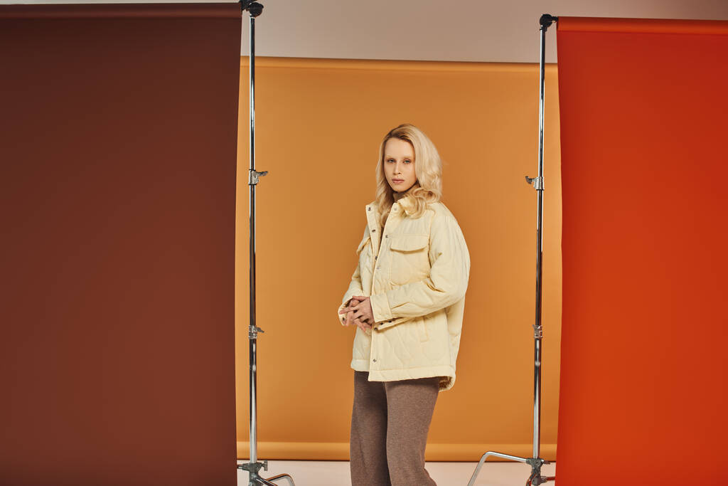 Осенняя мода, привлекательная женщина в осеннем наряде смотрит в камеру и позирует на оранжевом фоне - Фото, изображение