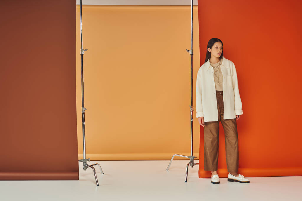 стильна азіатська жінка в осінньому вбранні стоїть на різнокольоровому тлі, шкіряні штани та верхній одяг - Фото, зображення