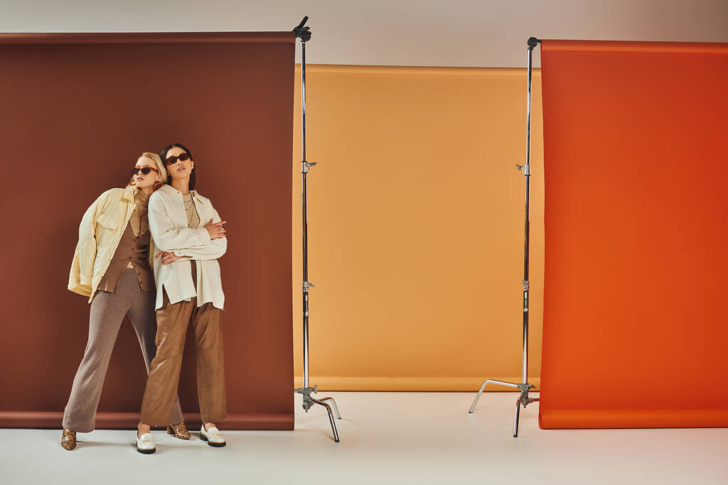 podzimní sezóna, multietnické modely ve slunečních brýlích a podzimní svrchní oděv pózující na barevném pozadí - Fotografie, Obrázek
