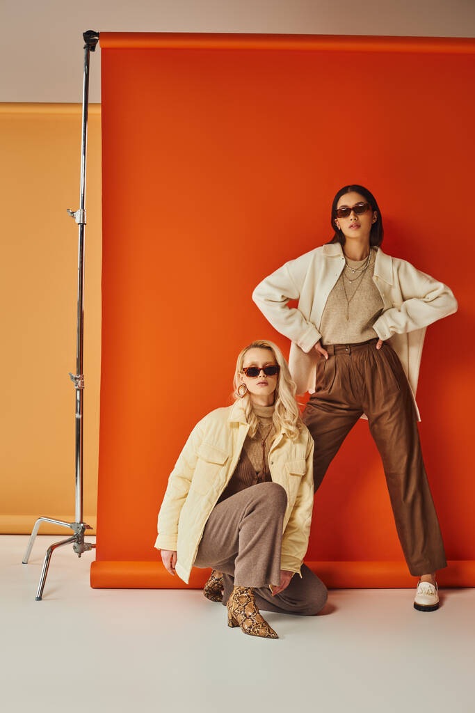 Mode und Trends, interrassische Frauen in Sonnenbrille und Oberbekleidung posieren im Studio, Herbstfarben - Foto, Bild
