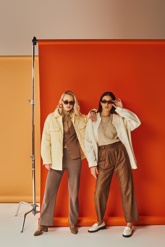 moda y estilo, modelos multiétnicos en gafas de sol y ropa de abrigo posando en estudio, colores de otoño - Foto, imagen