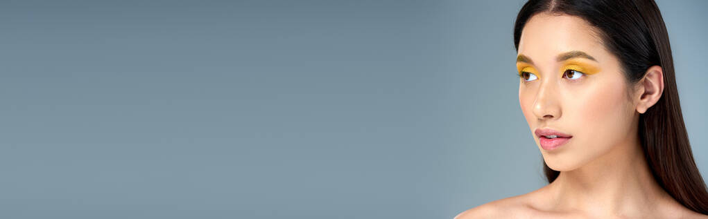 αίγλη, Ασιάτισσα γυναίκα με τολμηρό μακιγιάζ και γυμνούς ώμους κοιτάζοντας μακριά στο μπλε φόντο, λάβαρο - Φωτογραφία, εικόνα