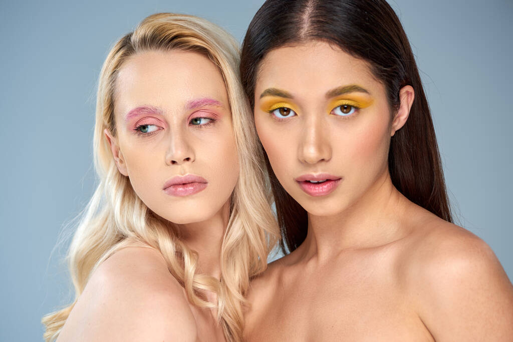 beauté diverse, portrait de deux modèles multiculturels avec un maquillage vibrant posant sur fond bleu - Photo, image