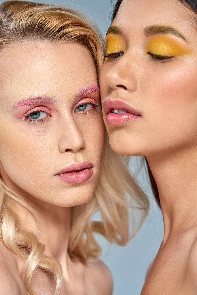 Diversifiziertes Schönheitskonzept, interrassische Frauen mit lebendigem Augen-Make-up posieren gemeinsam vor blauem Hintergrund - Foto, Bild