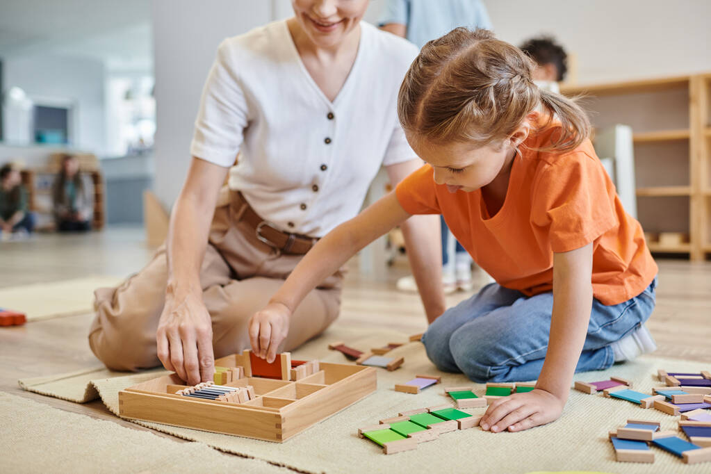 montessori school concept, meisje spelen kleur matching spel in de buurt van vrouwelijke leraar, zitten op de vloer - Foto, afbeelding