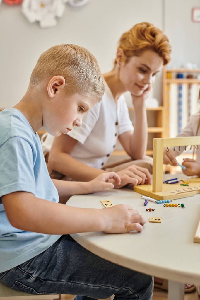 escuela montessori, niños jugando juego educativo, aprendizaje matemático, niño contando mientras mira azulejos - Foto, imagen