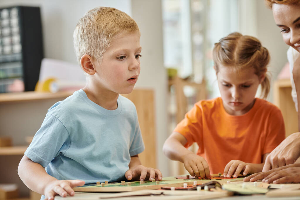 αγόρι κάθεται κοντά στο δάσκαλο και διδακτικό υλικό κατά τη διάρκεια του μαθήματος στο σχολείο Montessori - Φωτογραφία, εικόνα
