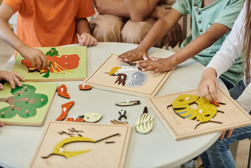 обрізаний вид міжрасових дітей, які грають з дидактичними матеріалами поблизу вчителя в школі Монтессорі - Фото, зображення