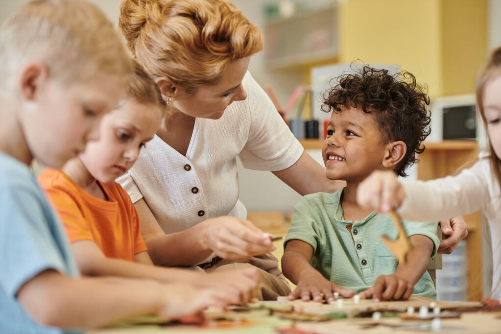 вчителька розмовляє зі усміхненим афроамериканським хлопчиком, коли діти грають у школі Монтессорі - Фото, зображення