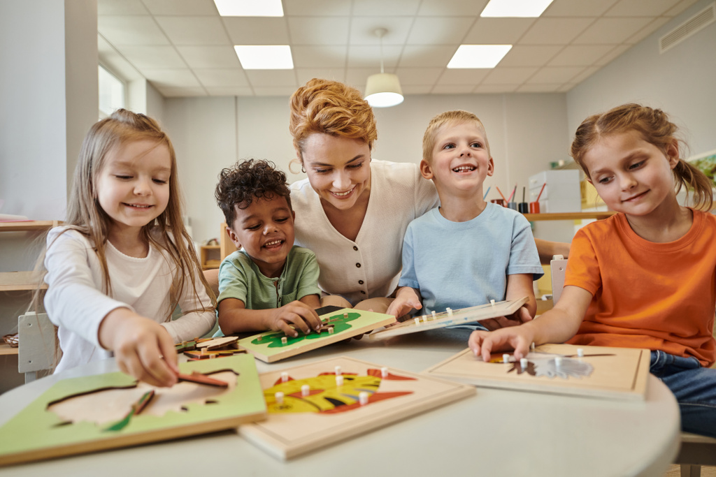 professor alegre sentado perto de crianças multiétnicas brincando com material didático na aula de montessori - Foto, Imagem