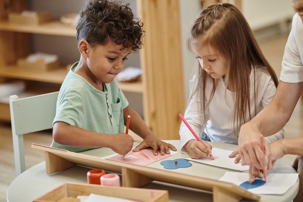 πολυεθνική παιδιά σχέδιο με μολύβια κοντά στο δάσκαλο κατά τη διάρκεια του μαθήματος στο Montessori σχολείο - Φωτογραφία, εικόνα